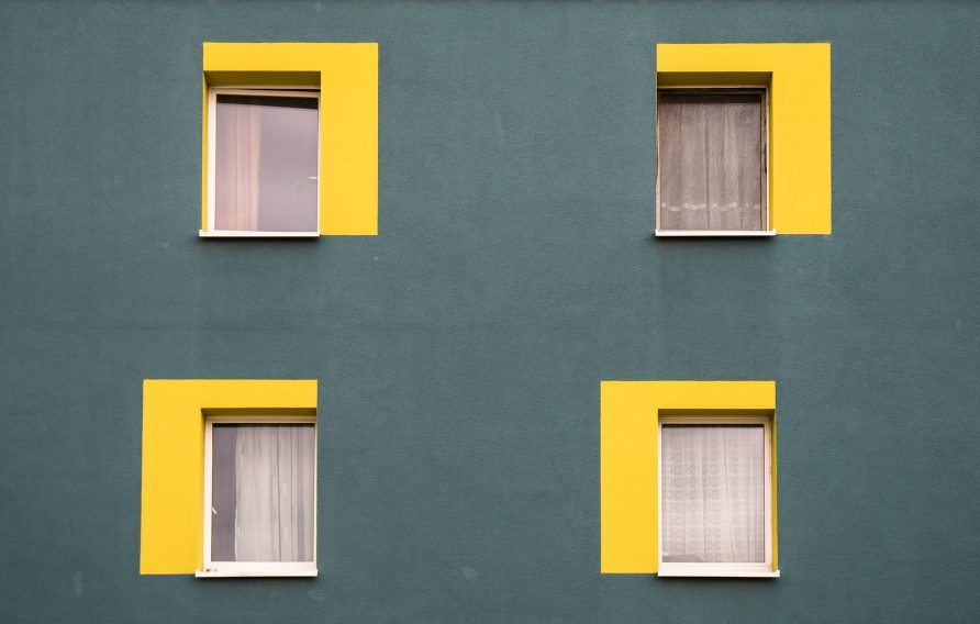 Vier gelb umrandete Fenster eines Hauses (Symbol für Grundverkehr beim Immobilienverkauf)